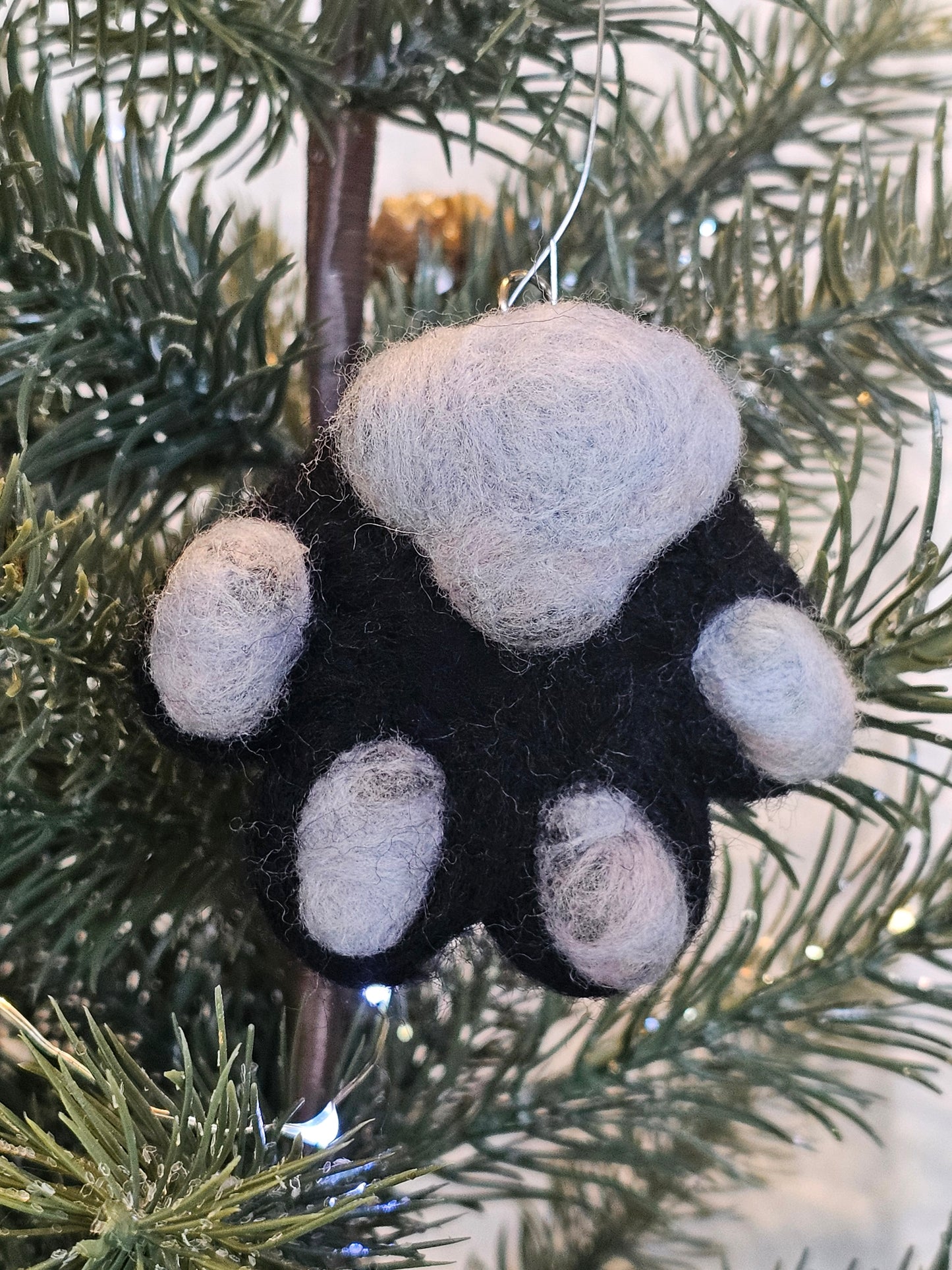 Needle-felted black cat paw with grey toe beans and a grey paw pad. Pictured hanging as an ornament in a tree.
