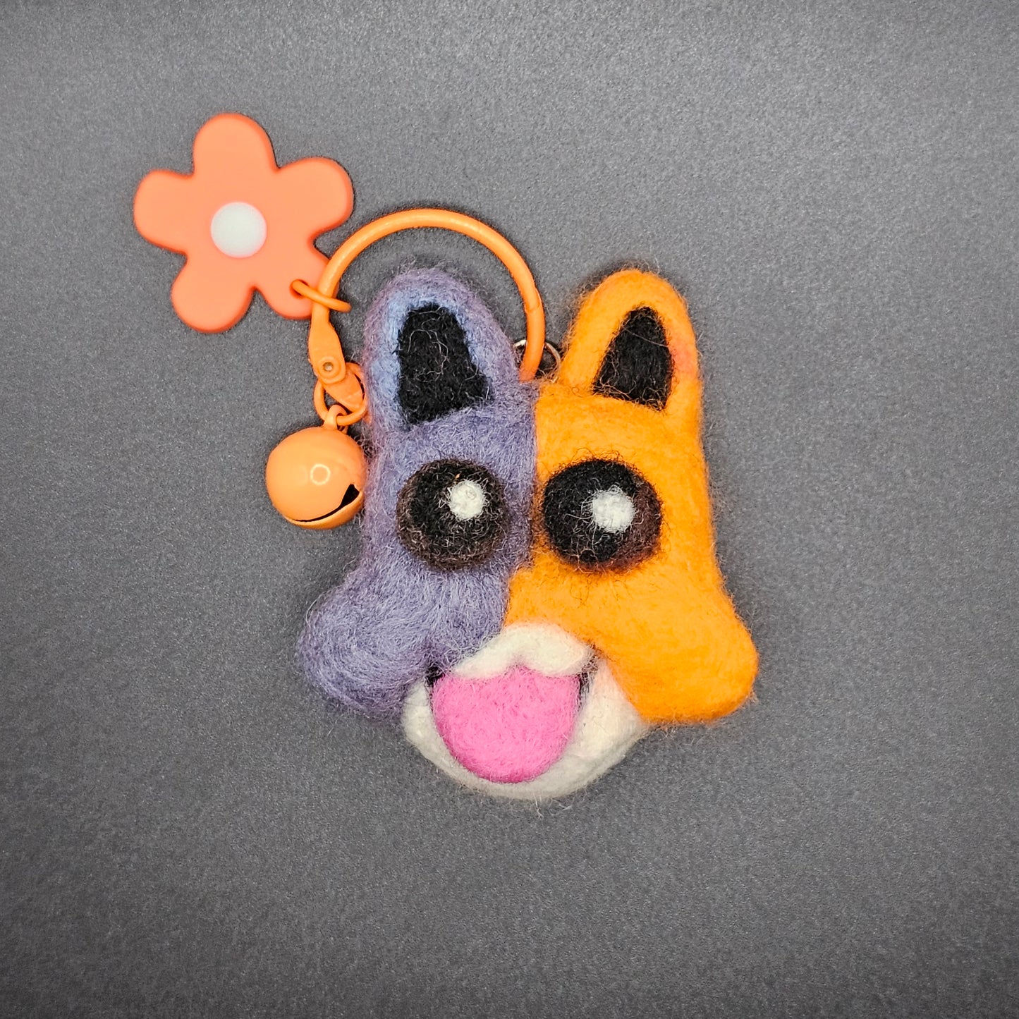 Meowscles' head on a keychain with an orange flower charm. Meowscles' is making an open-mouthed smile.