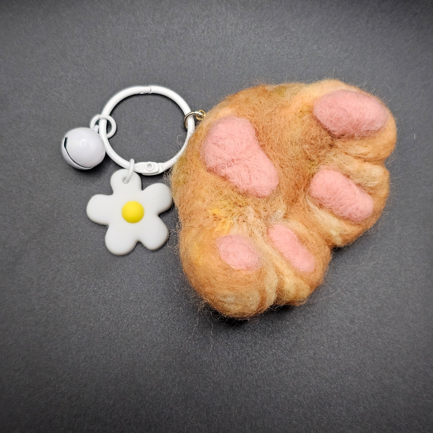 Needle-felted Orange cat paw with pink toe beans and paw pad. Pictured as keychain with white keyring and white flower charm.