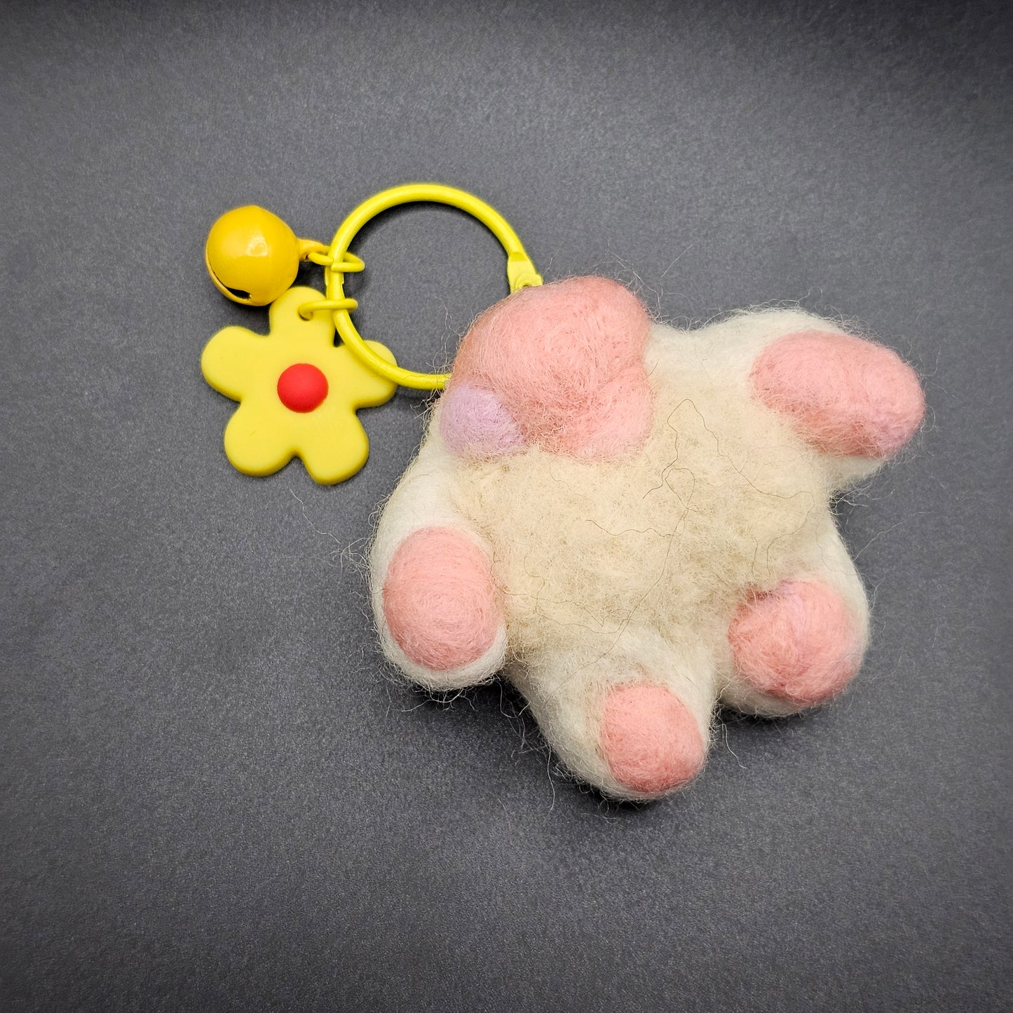 Needle-felted white cat paw with pink toe beans and pink paw pad. Pictured as a keychain with yellow keyring and yellow flower charm.