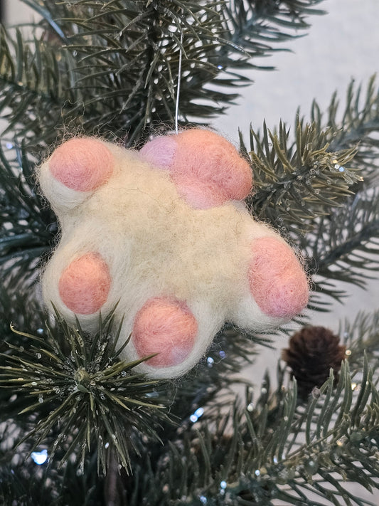 Needle-felted white cat paw with pink toe beans and pink paw pad. Pictured as ornament in a tree.