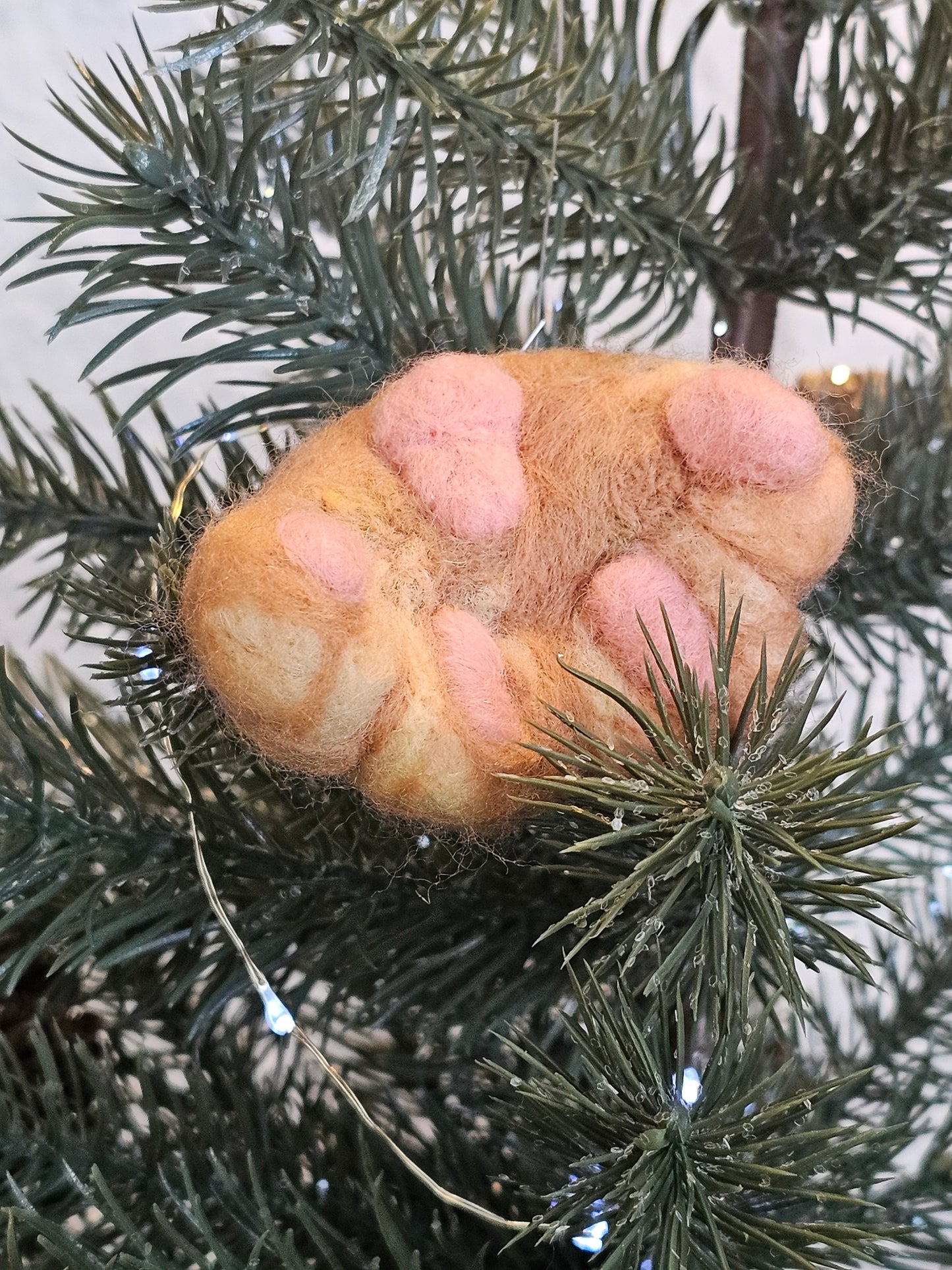 Needle-felted Orange cat paw with pink toe beans and paw pads. Photographed as an ornament in a tree.