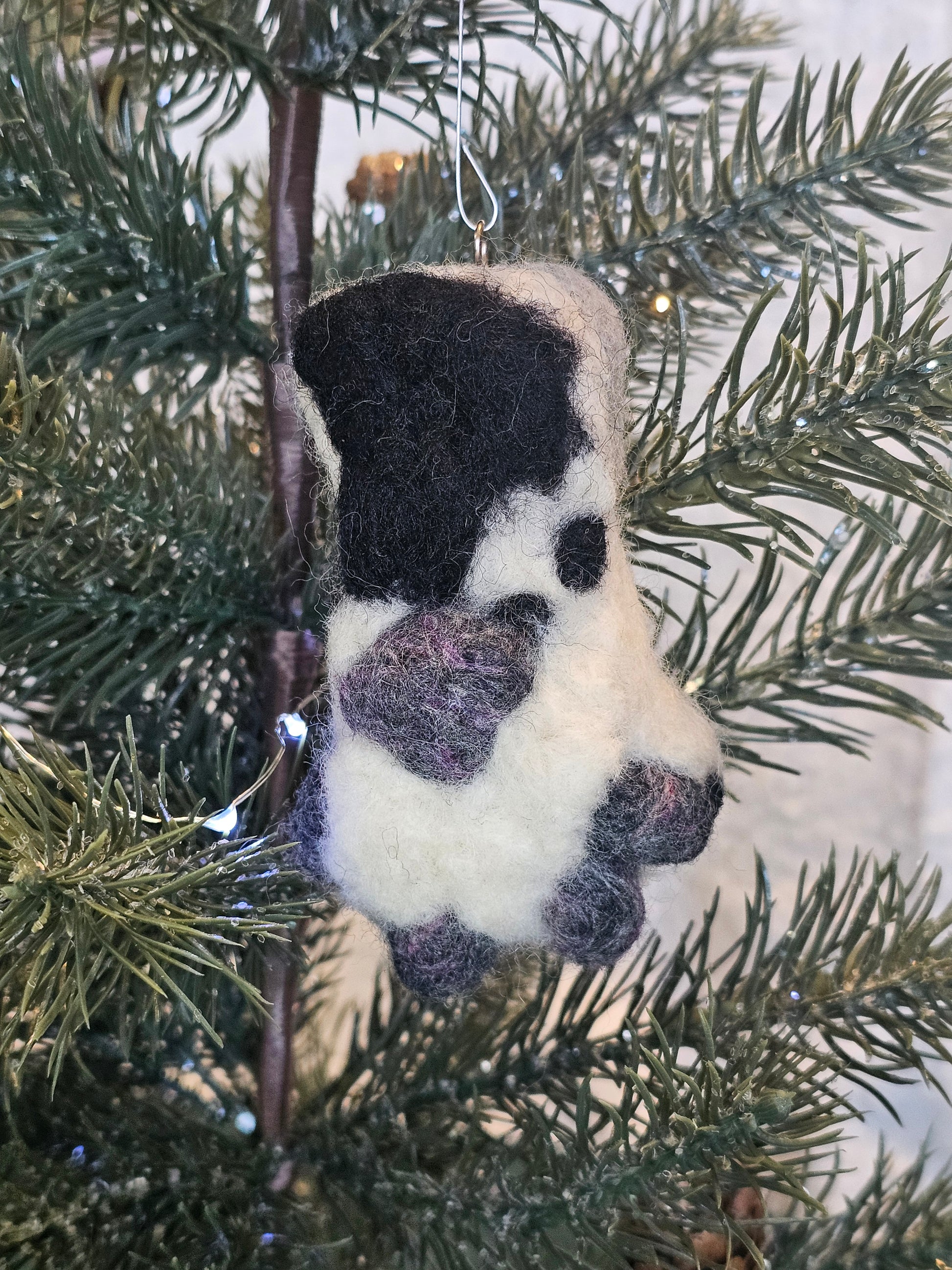 White fluffy paw with grey and pink speckled toe beans and paw pad. Ankle is a lighter grey with a large black spot. Pictured as tree ornament.