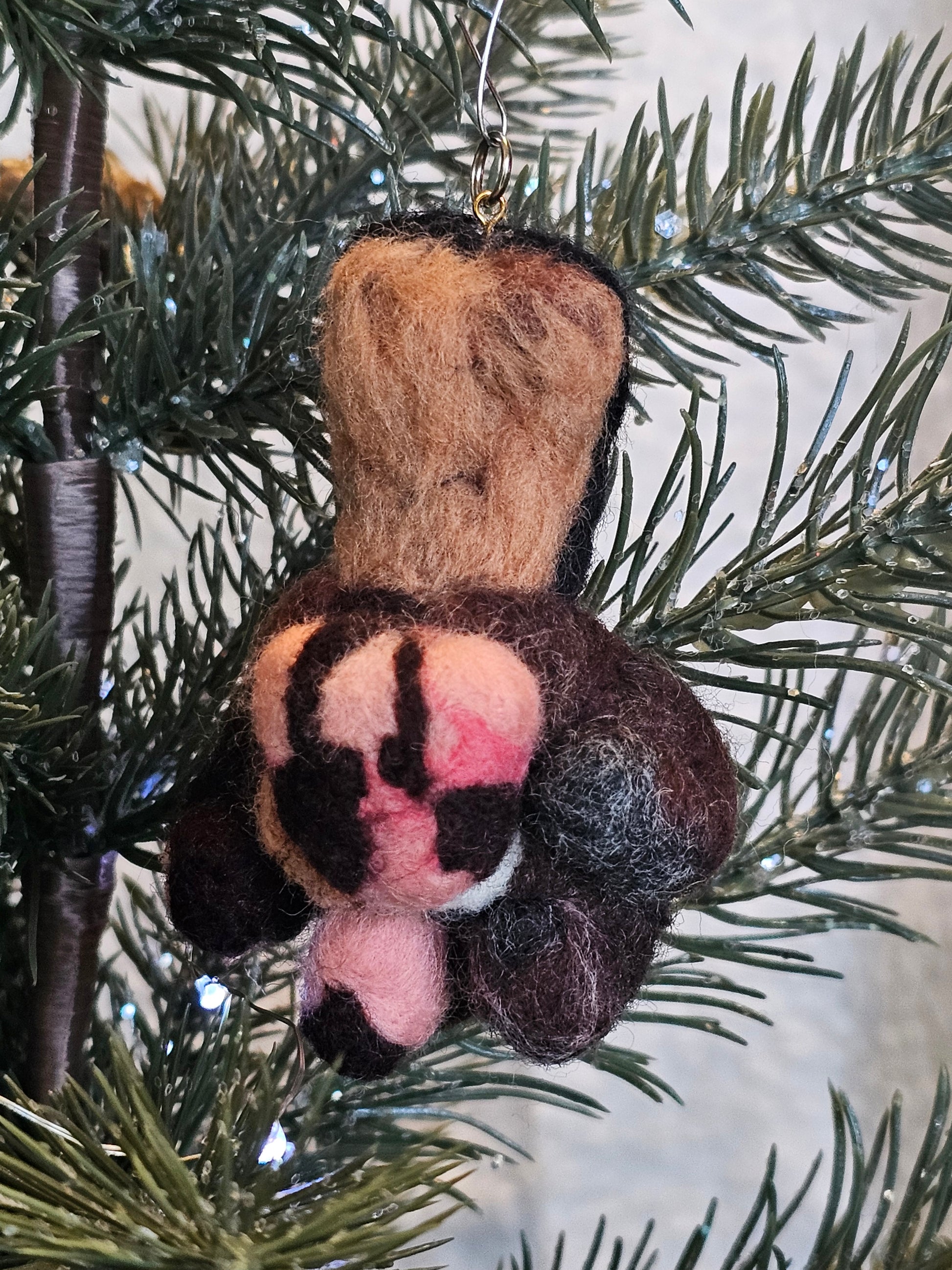 Needle-felted Tortoise Shell cat paw. Toe beans are brown, pink with a brown freckle, brown, and black. Paw pad is pink with another shade of pink, and brown freckles. Pictured aa a tree ornament.