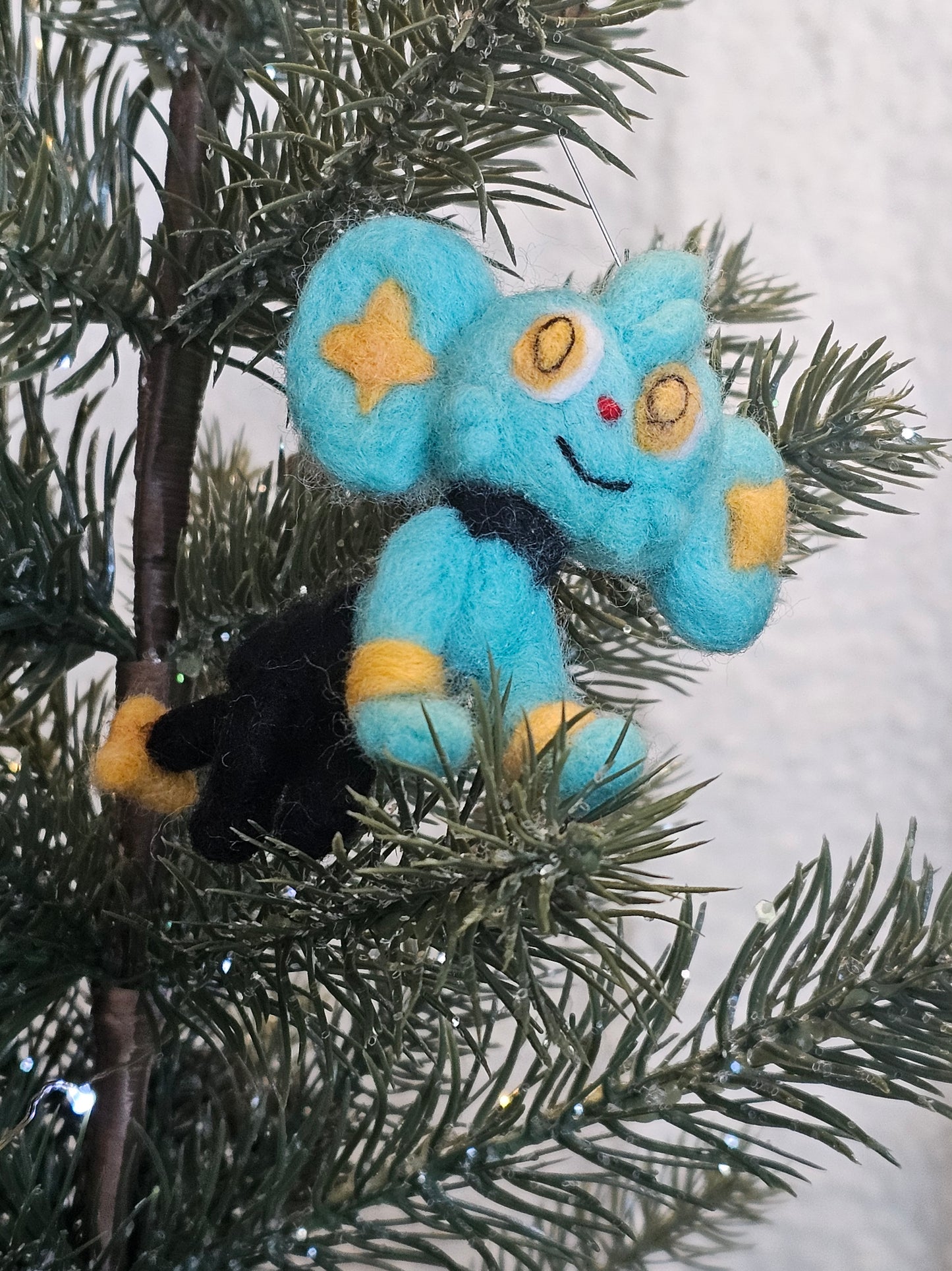 Shinx is a blue cat that looks like it's wearing black pants and a bow tie. He also has yellow stars in it's ears. Pictured as an ornament in a tree.
