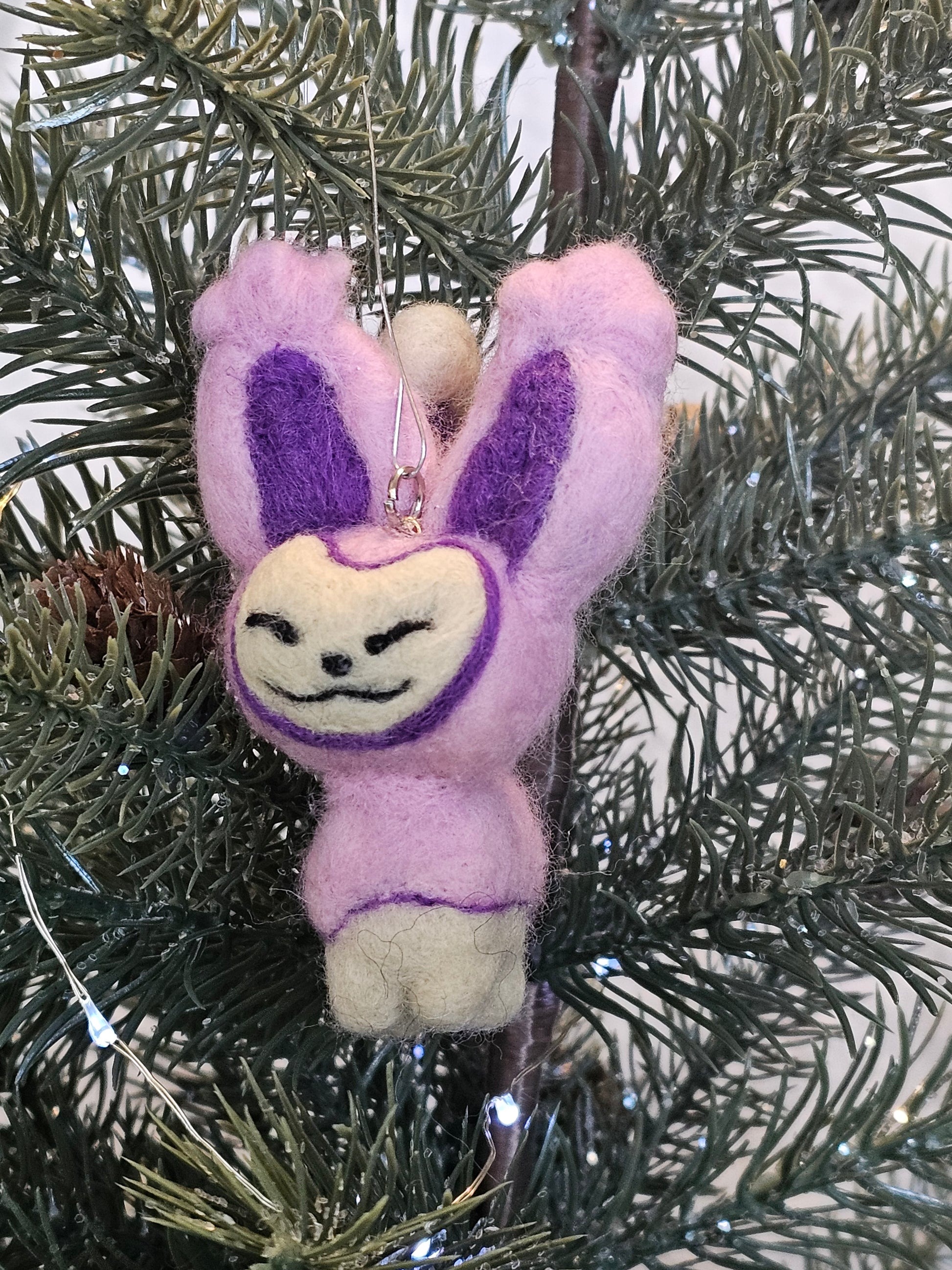 Skitty is a a pink cat with tall ears and a tail that looks sort of like a balloon on a string, with more balloons hanging from it. Features are outline with purple, and interior of ears is purple. Pictured as an ornament hanging in a Christmas tree.