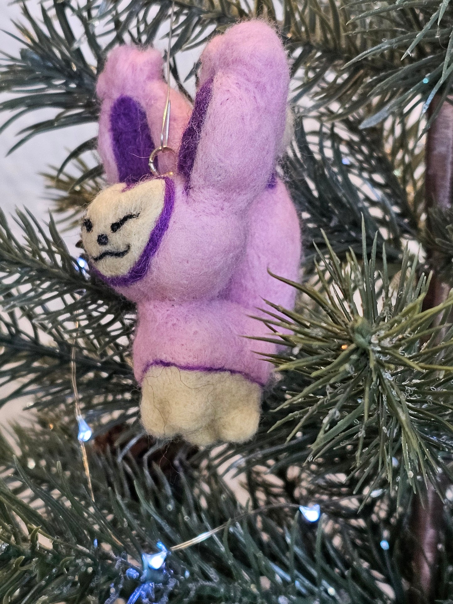 Skitty is a a pink cat with tall ears and a tail that looks sort of like a balloon on a string, with more balloons hanging from it. Features are outline with purple, and interior of ears is purple. Pictured as an ornament in the tree.