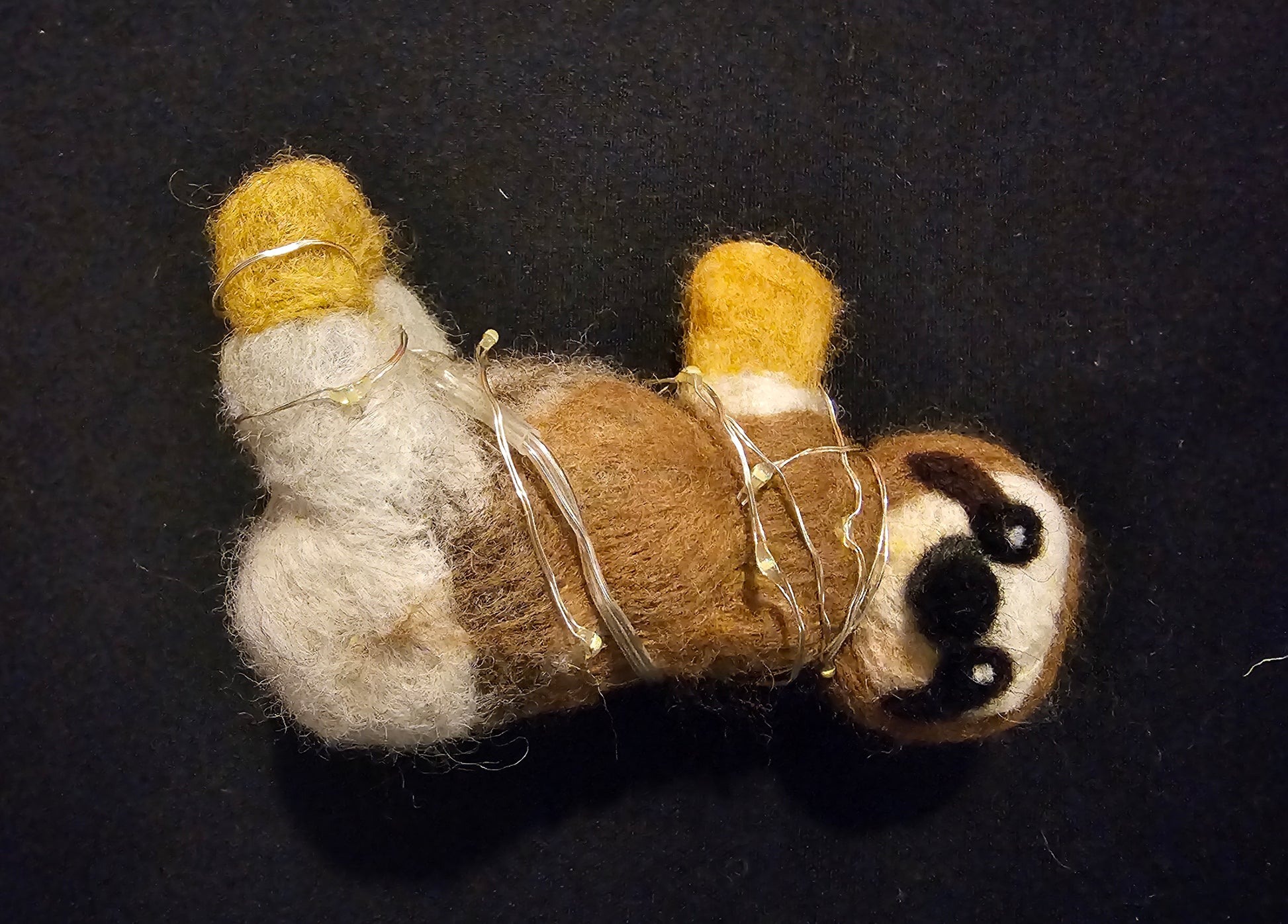 Needle-felted sloth laying on it'd back on a black background 
