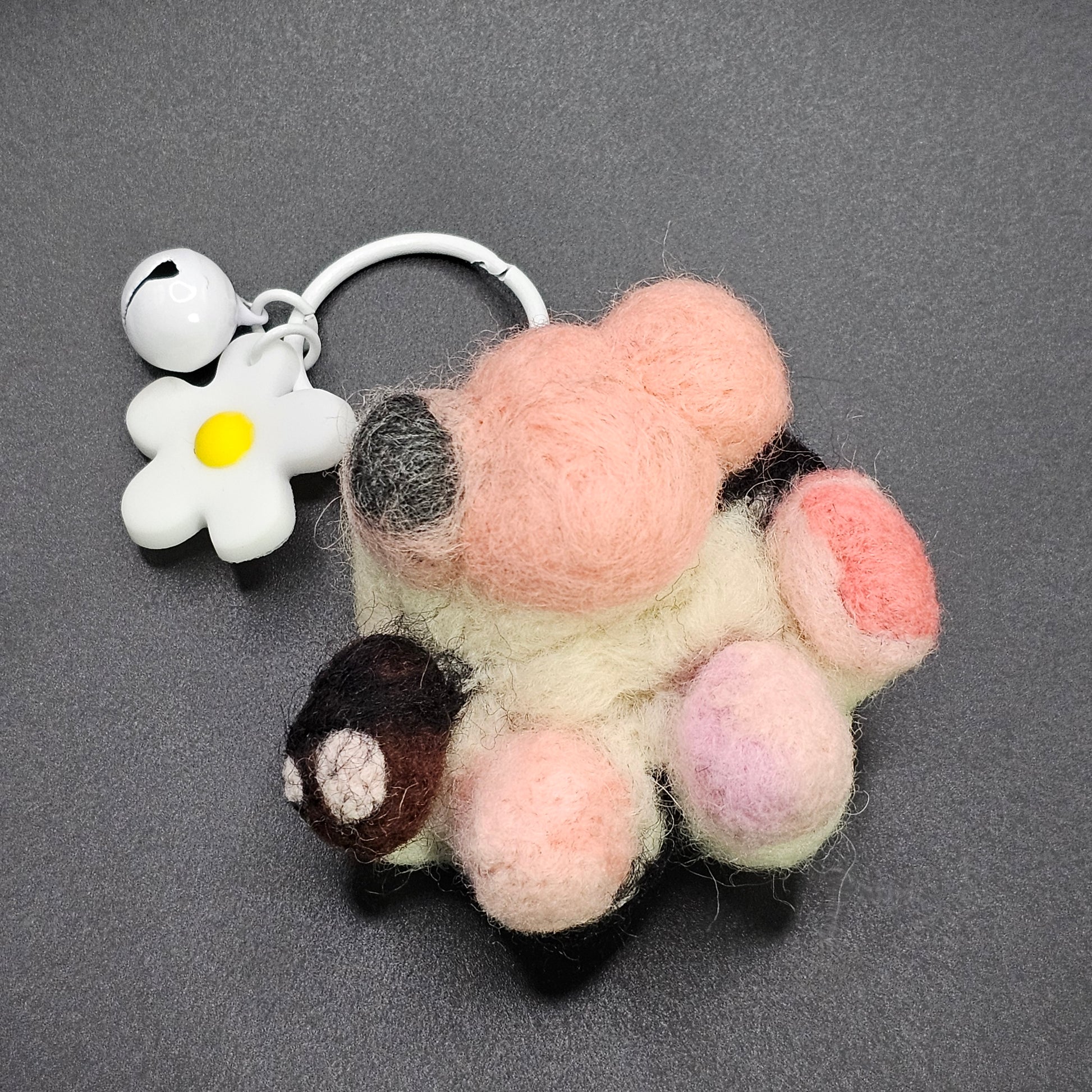 Needle-felted tortoise shell pet paw with a white keyring with a white flower charm. The paw has 3 pink beans with varying pink spots, and one black and brown bean with a couple pink spots. The paw pad has a grey spot.