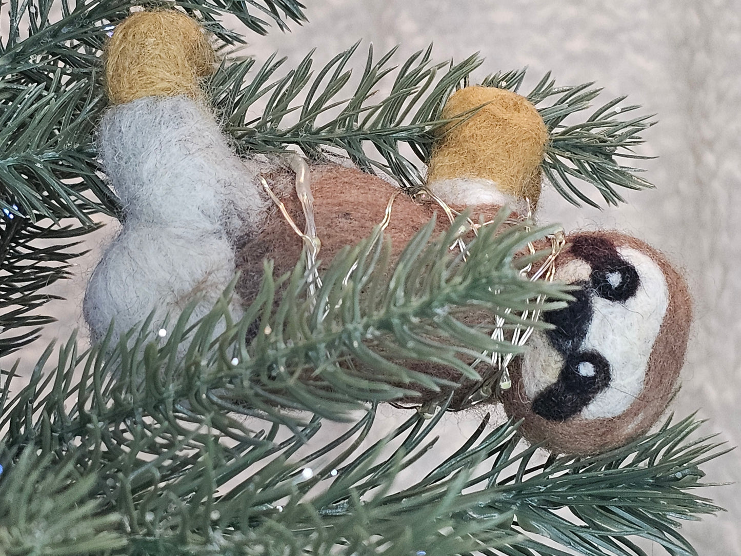Needle-felted sloth hanging on a tree branch