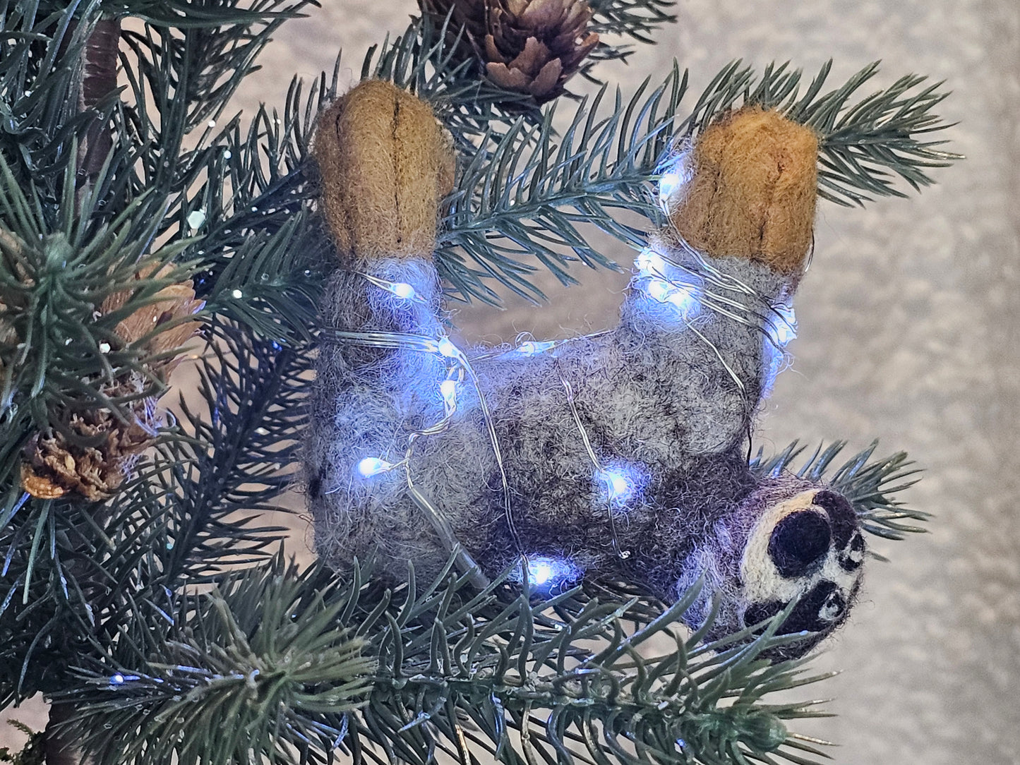 Needle-felted sloth hanging in tree from all fours. Twinkle lights are lit up.