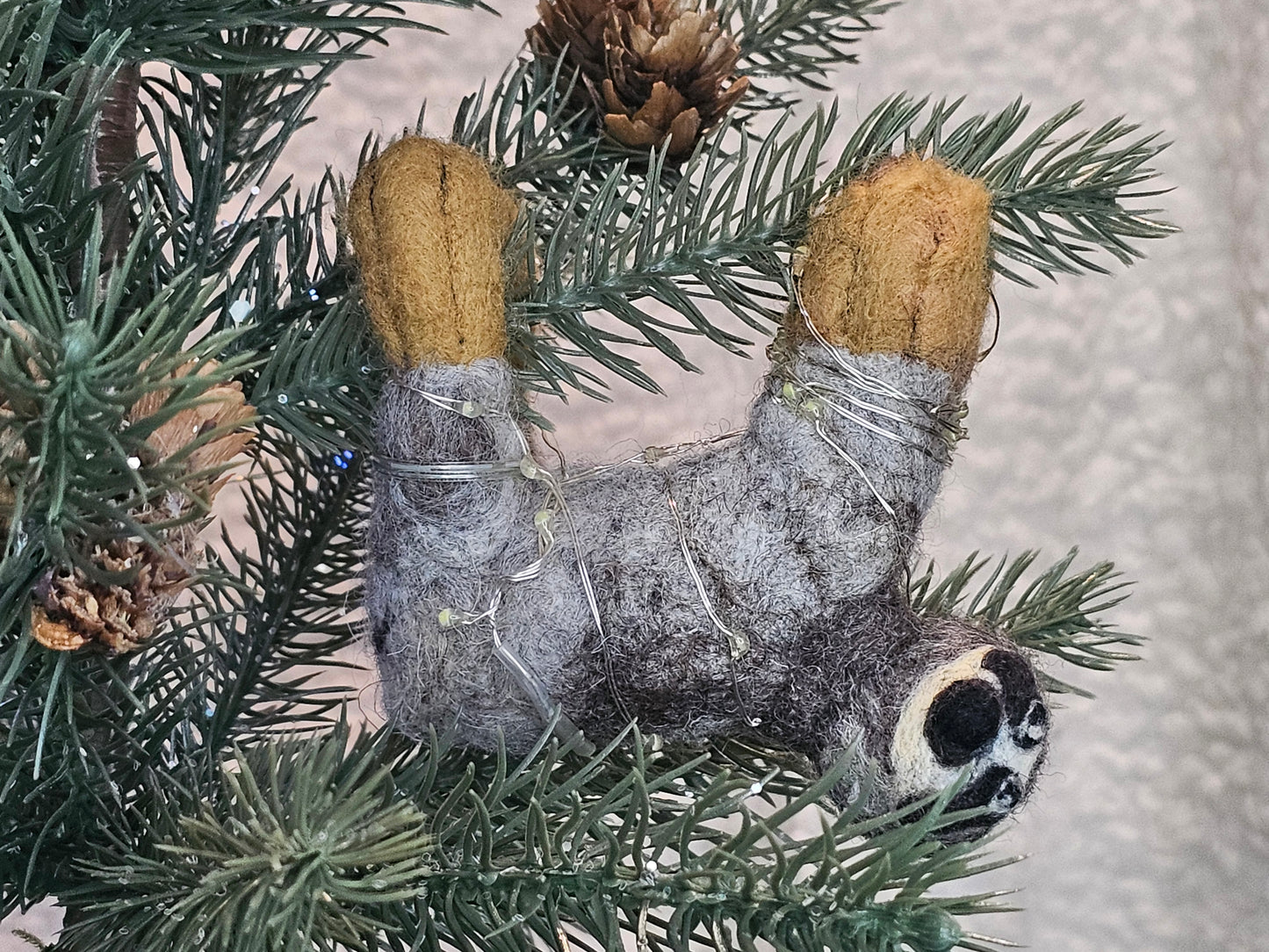 Needle-felted sloth hanging on a tree branch from all fours.
